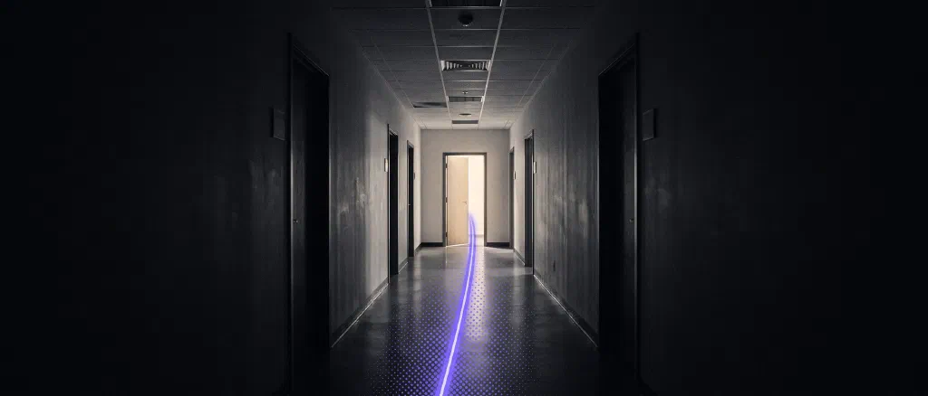A dark office corridor with a single violet streak of light running down the floor to one lit doorway