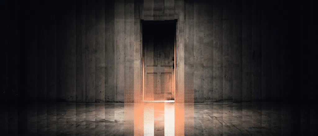 A tall wooden door in a concrete wall with a band of warm orange halftone light spilling from its lower gap