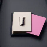 A stack of cream paper sheets with a small cut-out door, beside one thick pink sheet lifted out of the stack