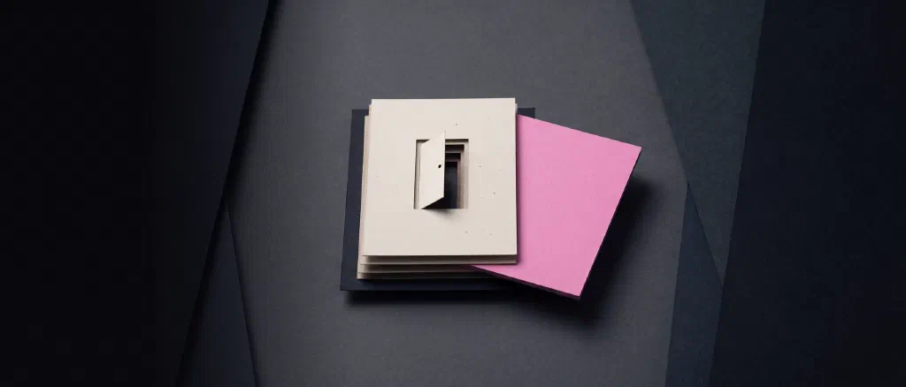 A stack of cream paper sheets with a small cut-out door, beside one thick pink sheet lifted out of the stack